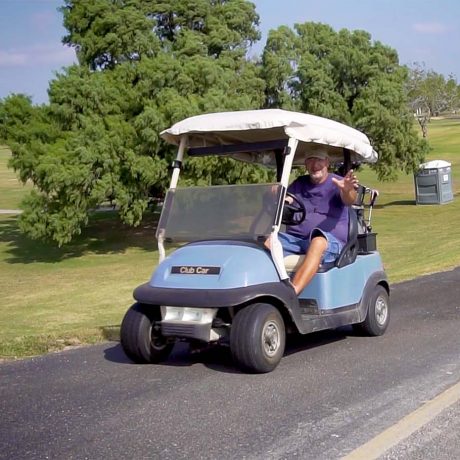man driving golf cart on golf course, waving